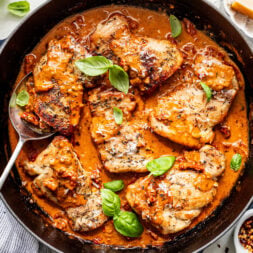 Chicken thighs simmered in a creamy tomato sauce with herbs, garnished with fresh basil leaves in a black skillet.