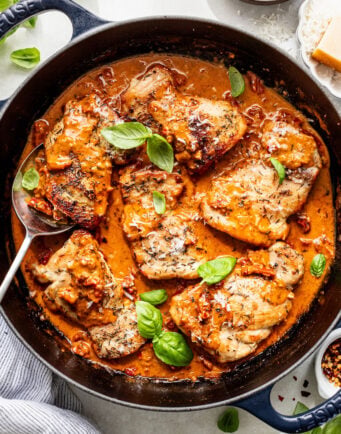 Chicken thighs simmered in a creamy tomato sauce with herbs, garnished with fresh basil leaves in a black skillet.
