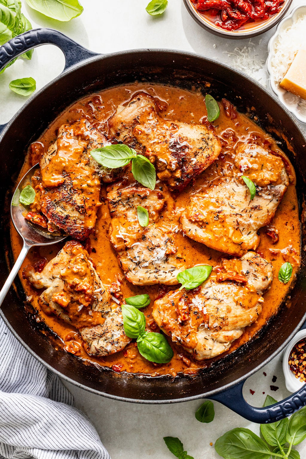 Chicken breasts simmered in a creamy tomato sauce with herbs, garnished with fresh basil leaves in a black skillet.