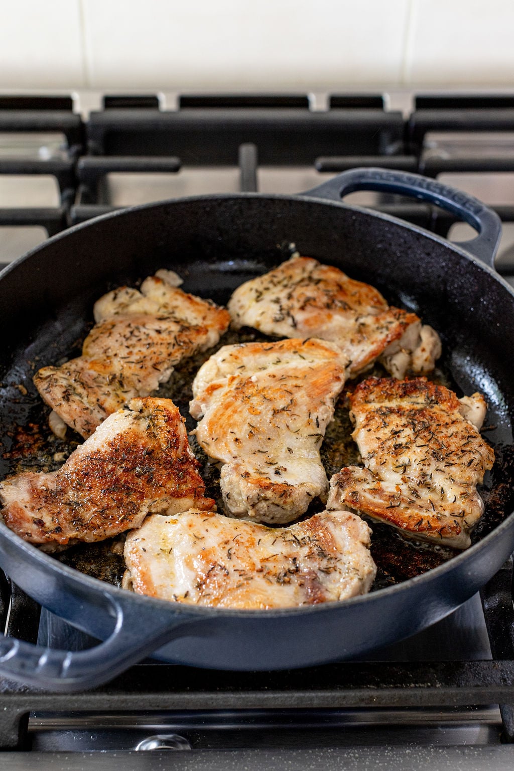Six seasoned chicken thighs are being pan-seared in a black cast iron skillet on a gas stovetop.