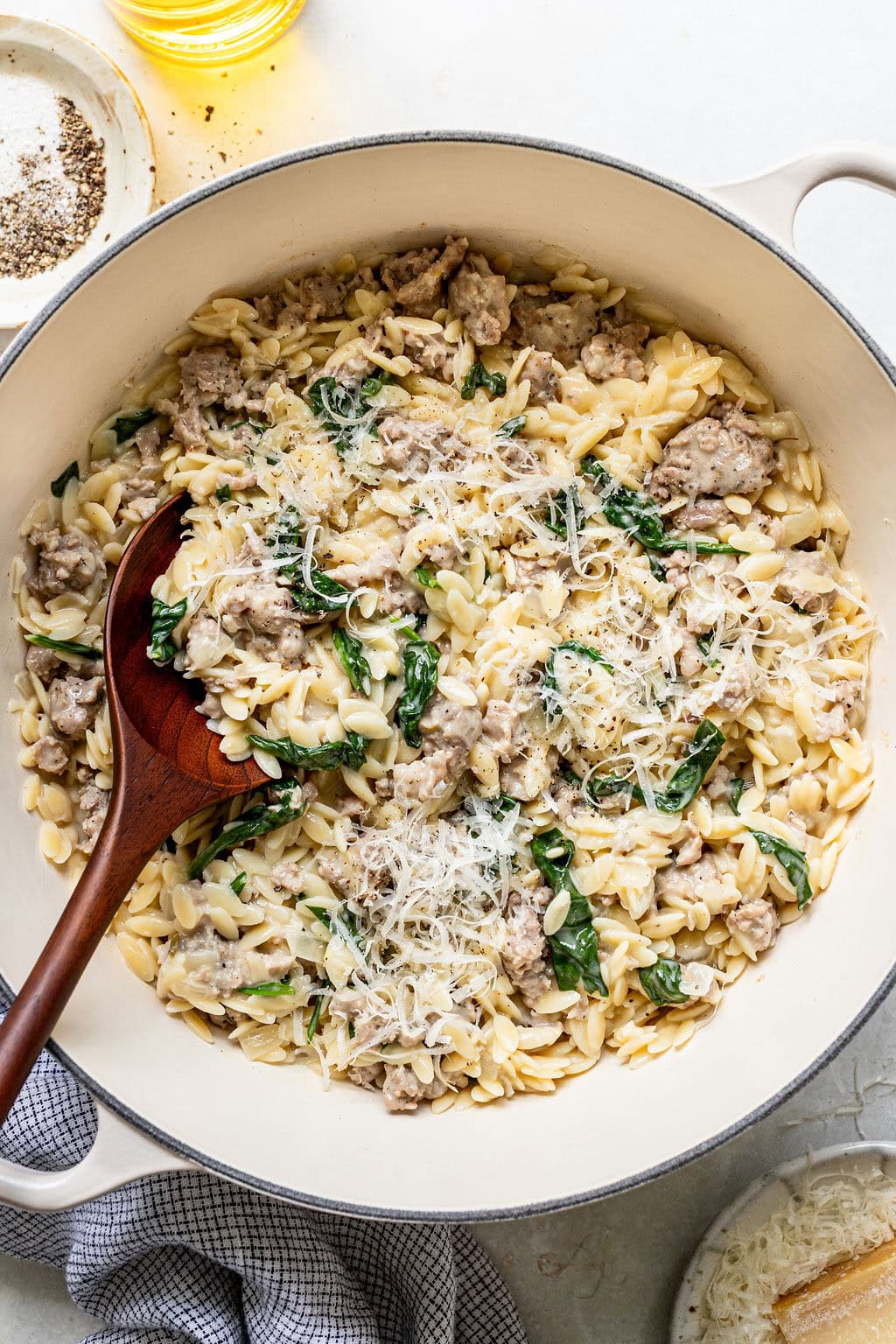 A large pot of orzo pasta mixed with sausage, spinach, and grated cheese, with a wooden spoon resting on the side.
