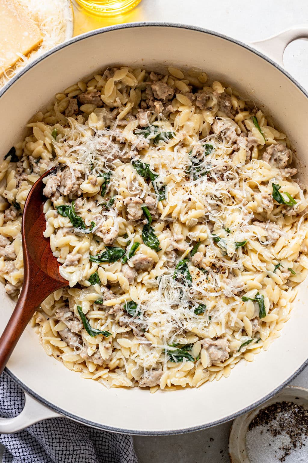 A pot of orzo pasta with ground meat, spinach, and grated cheese, mixed with a wooden spoon.