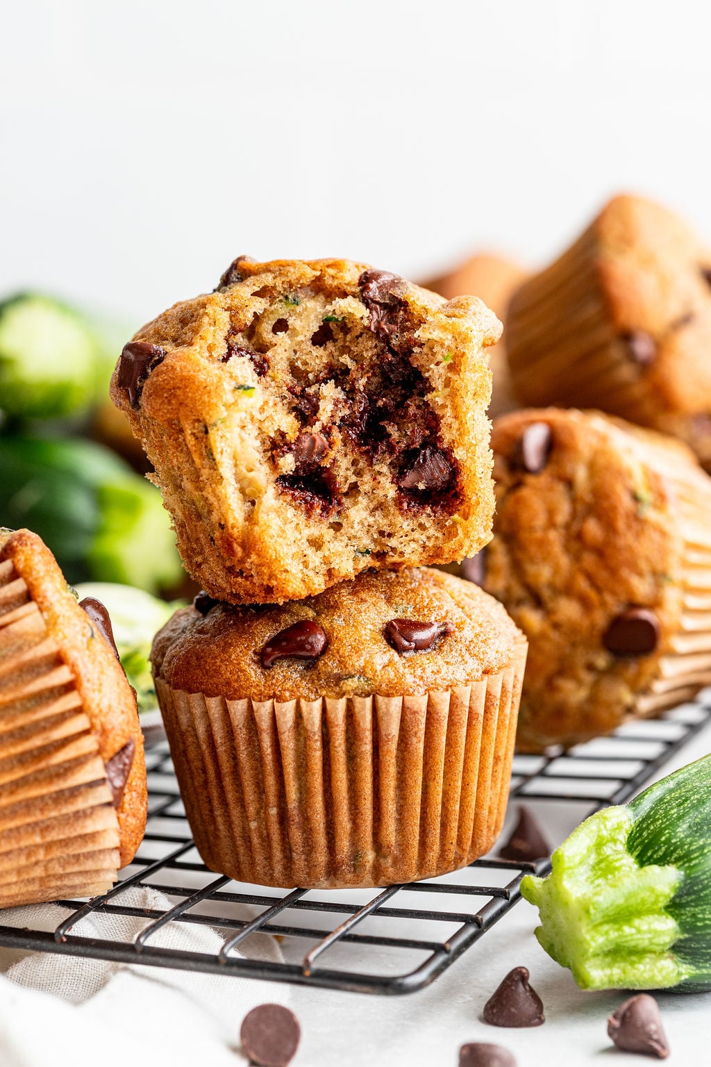 A stack of chocolate chip zucchini muffins sits on a cooling rack, with the top muffin broken open to show the chocolate chips inside.