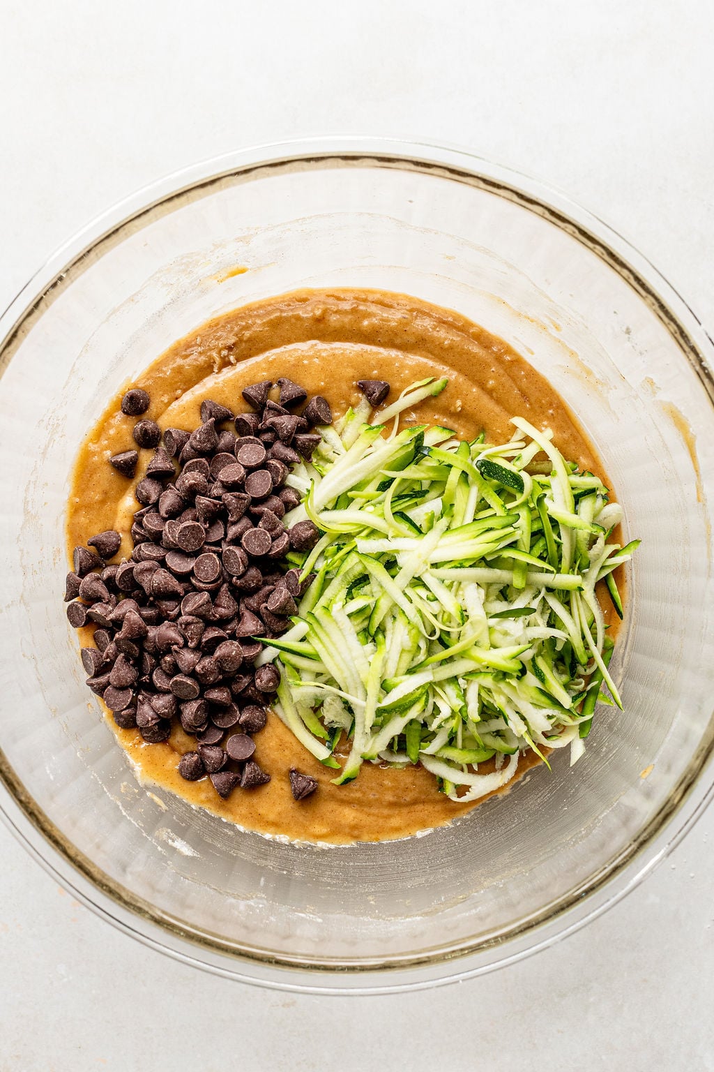 Glass bowl containing batter with shredded zucchini and chocolate chips on top, before mixing.