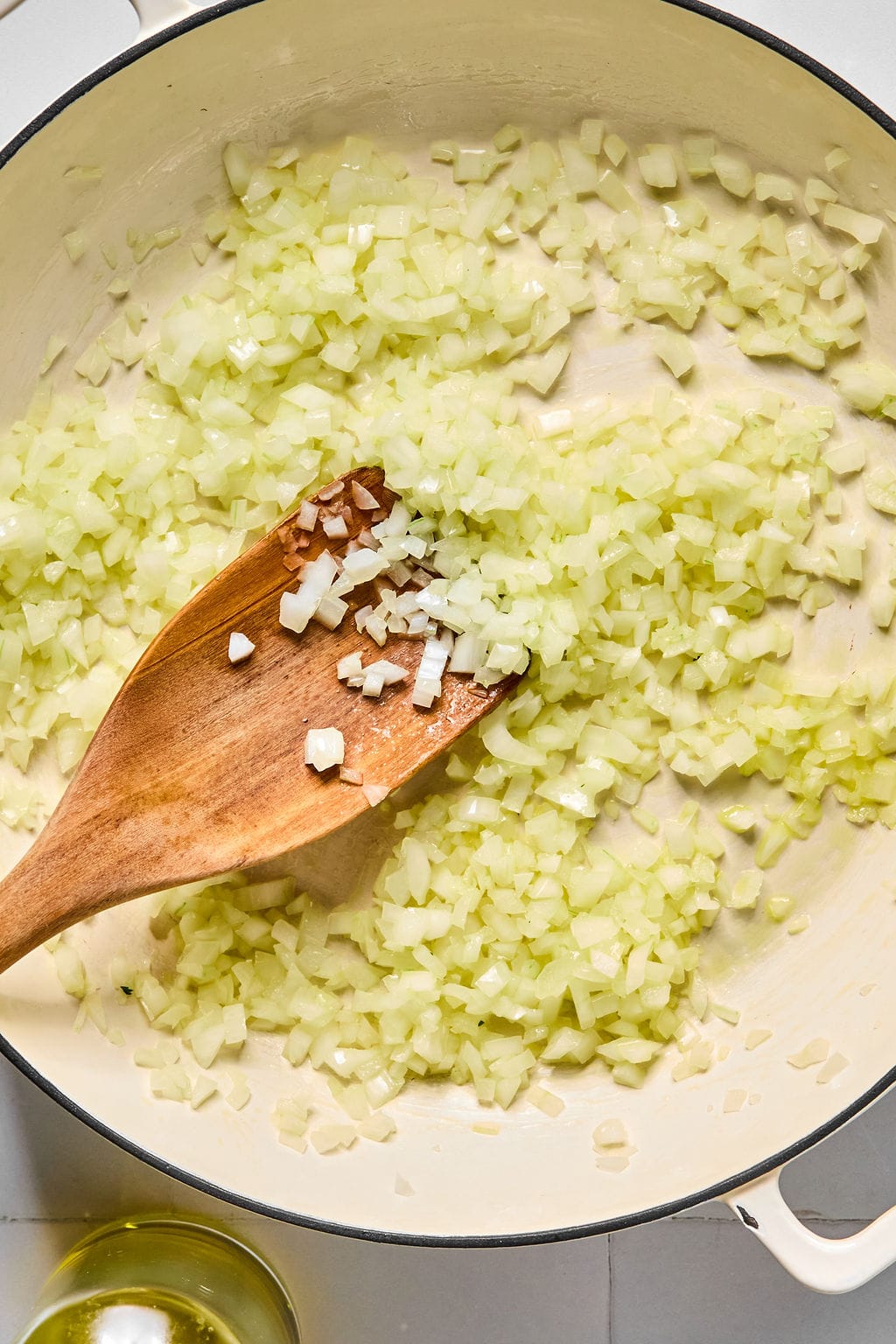 Diced onions being sautéed in a large pan, stirred with a wooden spatula.