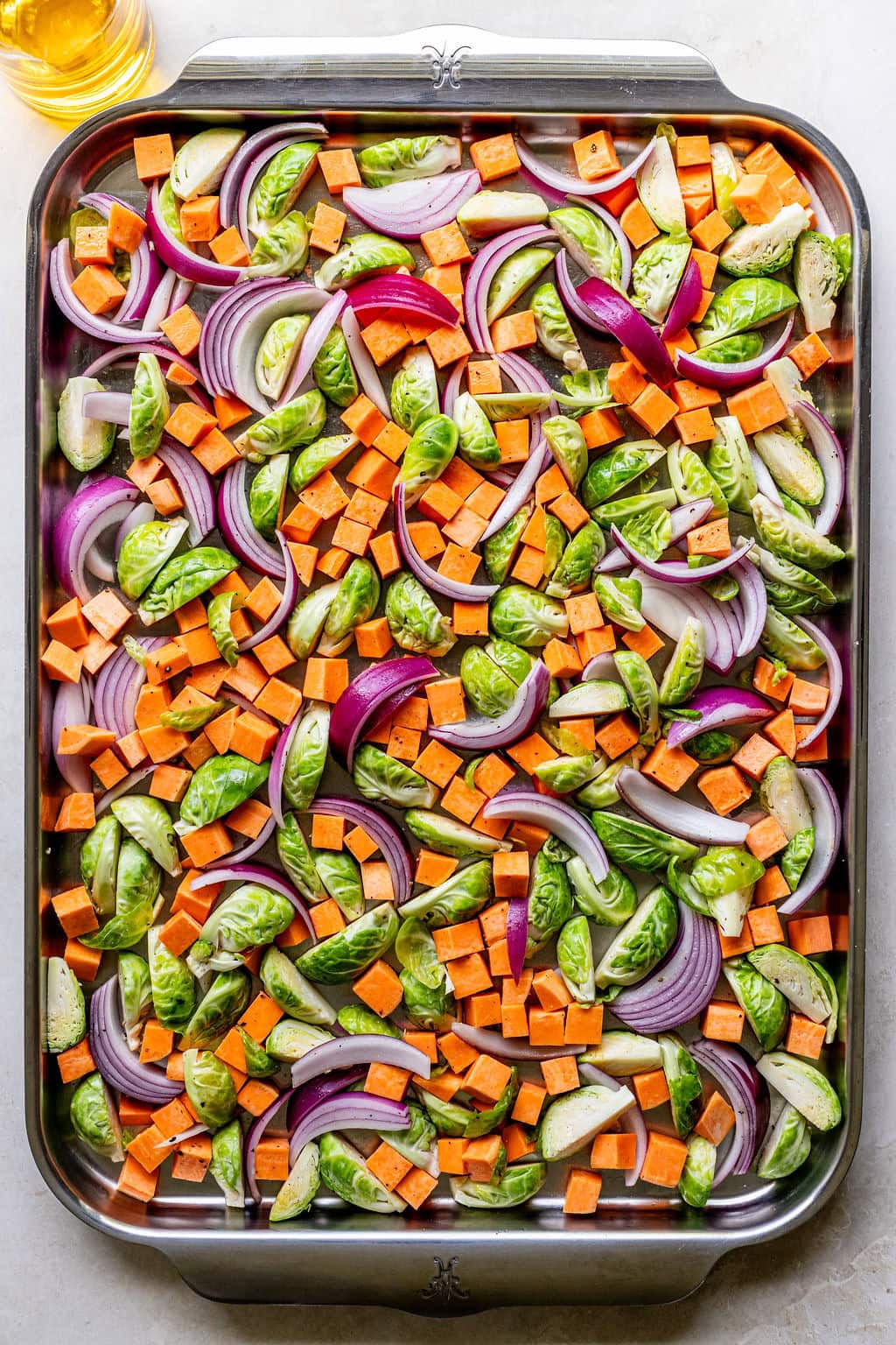 A baking sheet filled with chopped sweet potatoes, Brussels sprouts, and red onion slices, ready to be roasted.