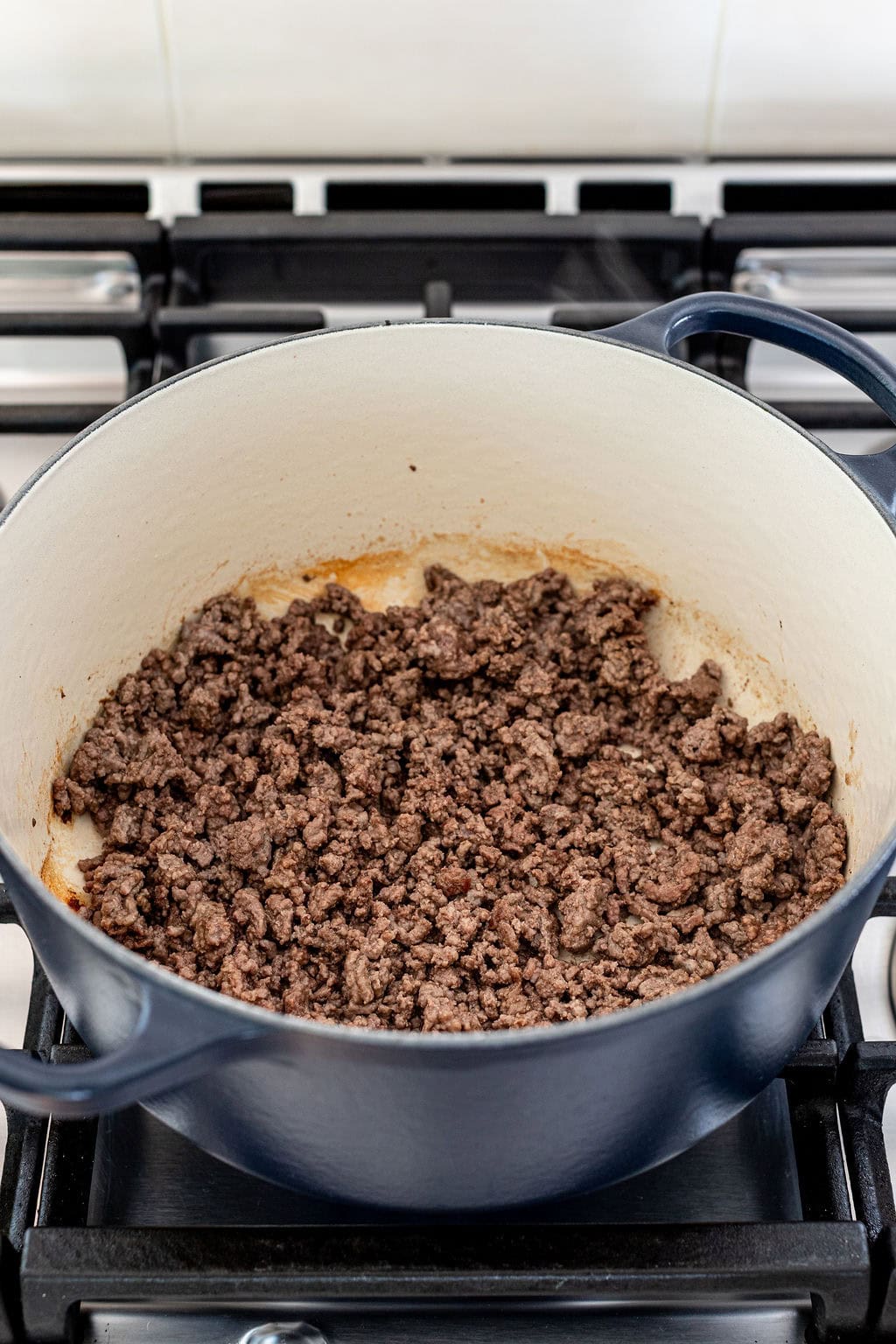 Cooked ground beef in a large blue Dutch oven sits on a gas stovetop, with browned bits visible.