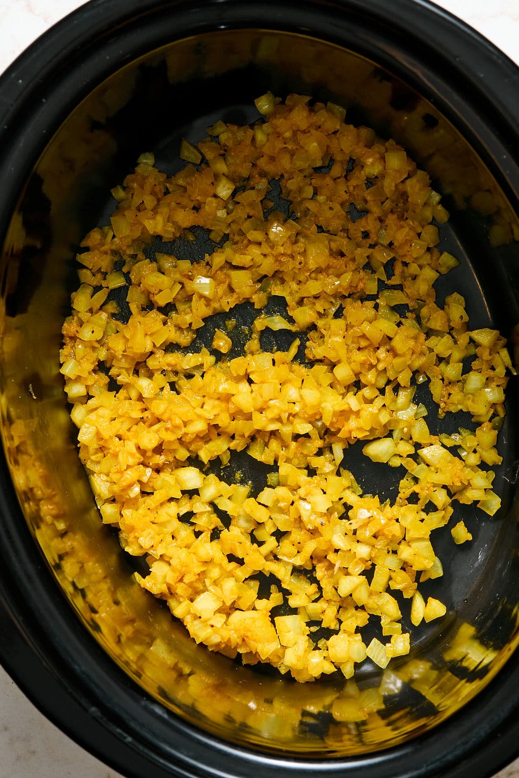 Diced yellow onions saut&eacute;ed with turmeric inside a black slow cooker.