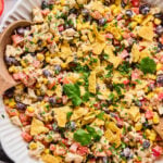 A white dish filled with a mixed salad of corn, black beans, diced vegetables, chicken, topped with crushed tortilla chips and garnished with cilantro.
