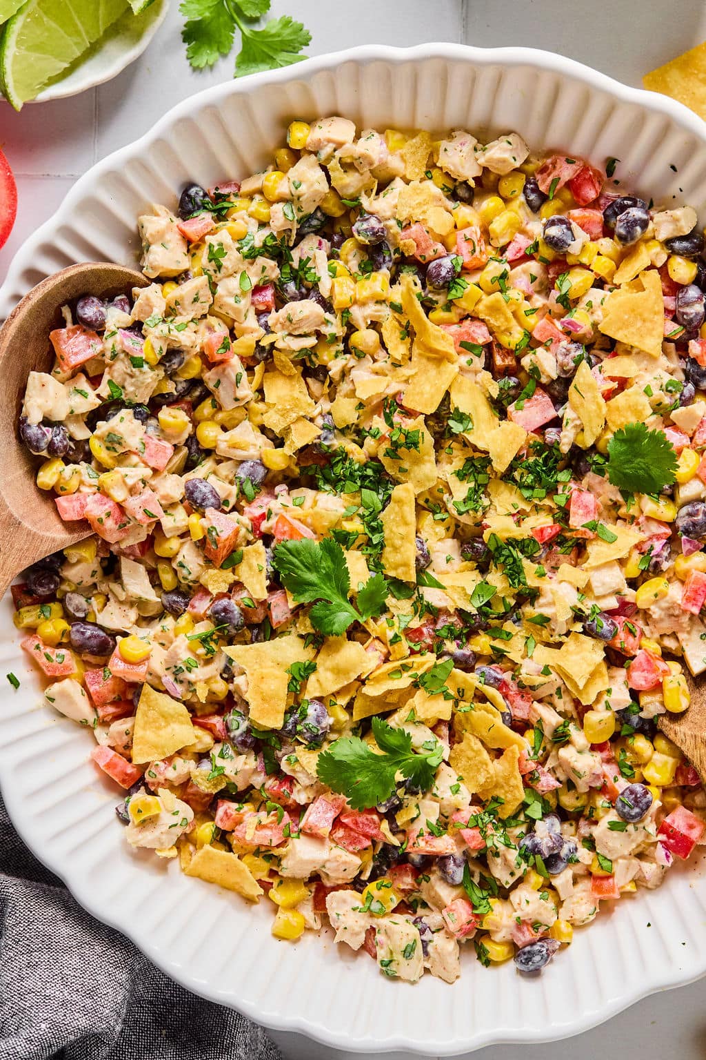 A white dish filled with a mixed salad of corn, black beans, diced vegetables, chicken, topped with crushed tortilla chips and garnished with cilantro.