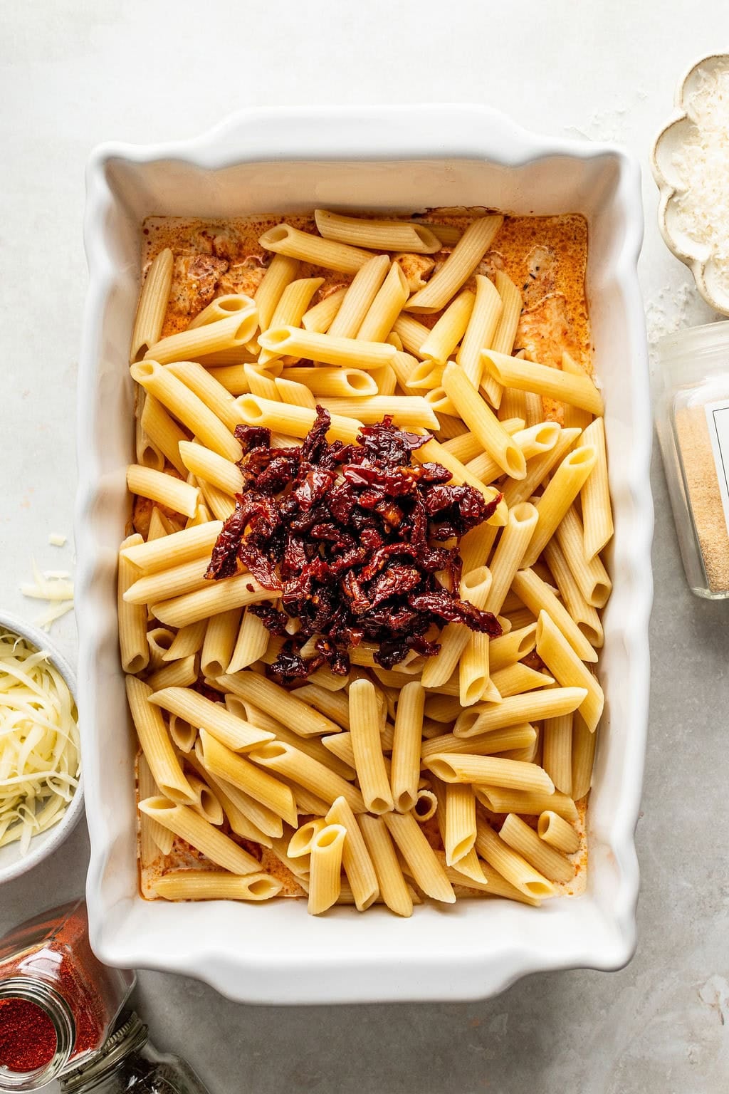 A rectangular baking dish filled with penne pasta and sun-dried tomatoes in a creamy sauce.