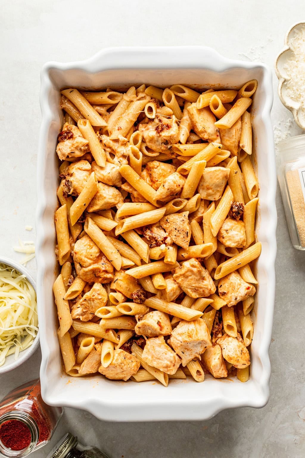 A white baking dish filled with penne pasta tossed in a creamy sauce with chicken pieces and sun-dried tomatoes.