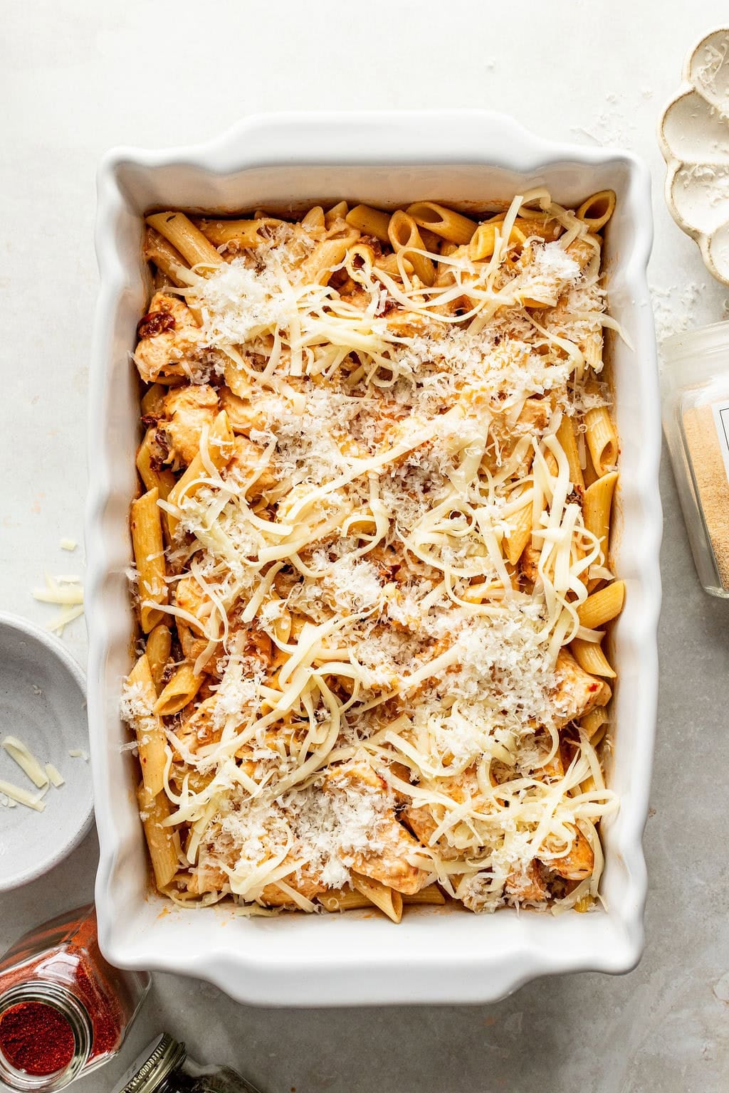 Baked penne pasta with chicken in a white casserole dish, topped with shredded cheese.