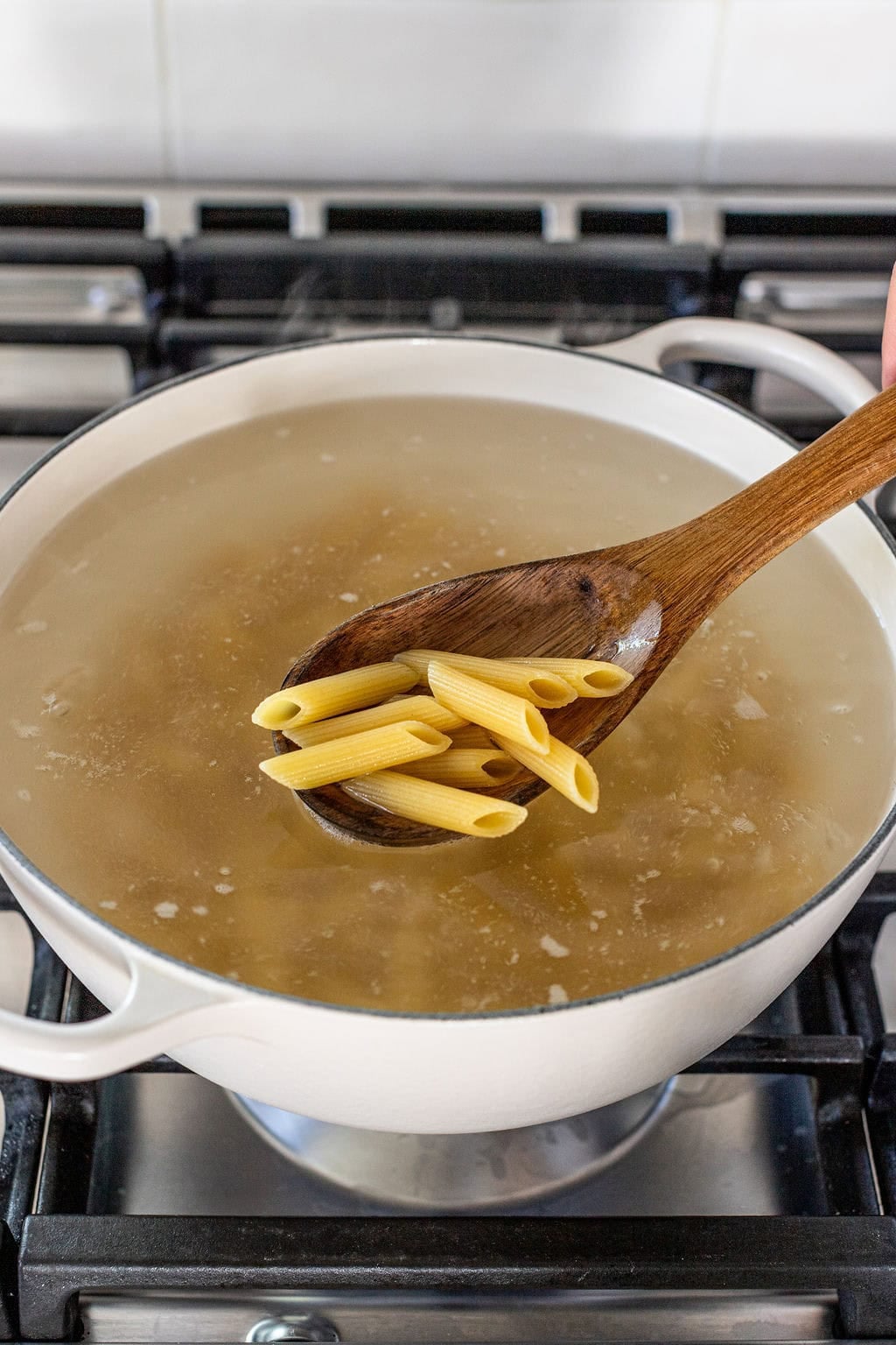 A wooden spoon lifting cooked penne pasta from a pot of boiling water.