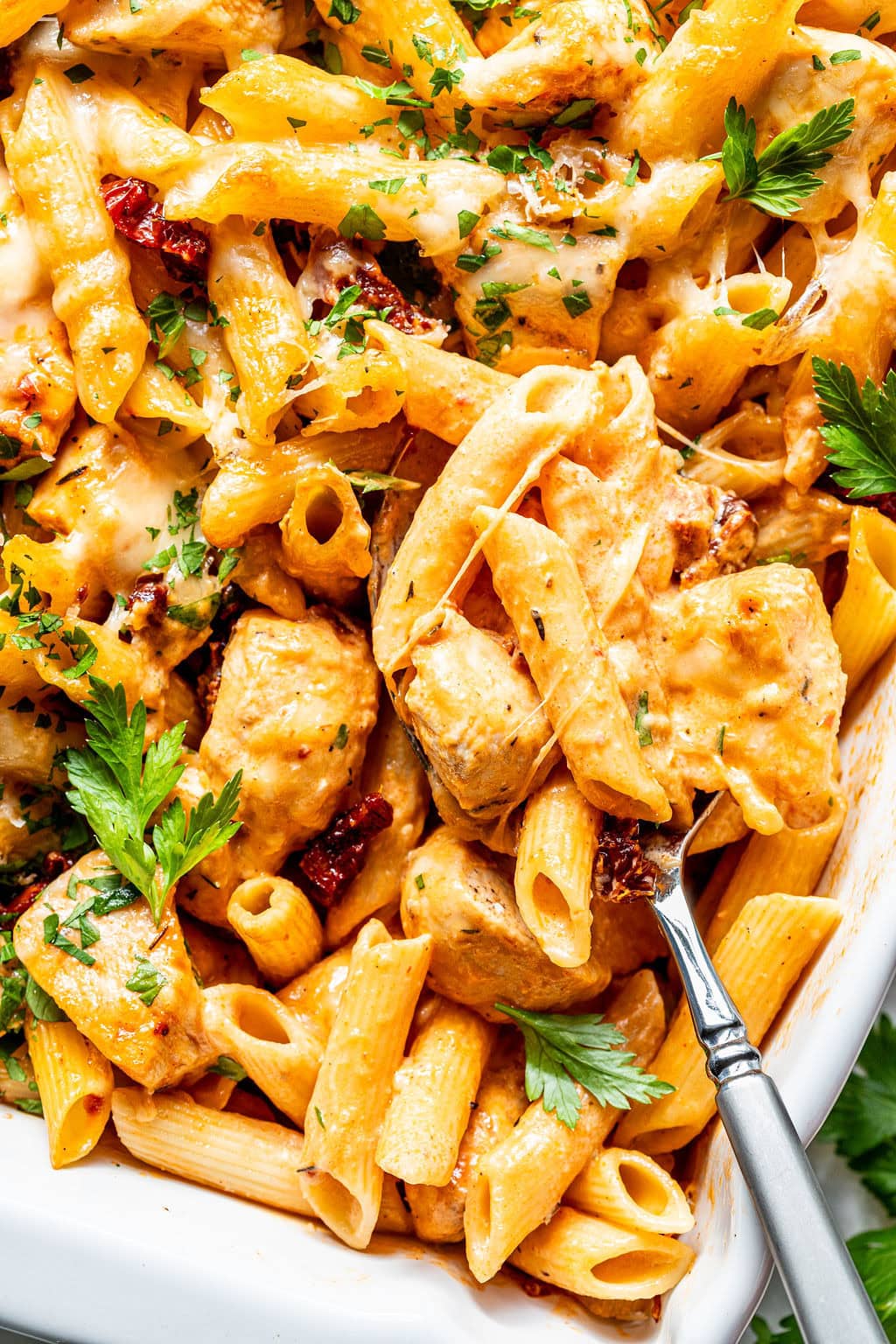 Penne pasta with chicken, sun-dried tomatoes, and melted cheese in a creamy sauce, garnished with parsley.