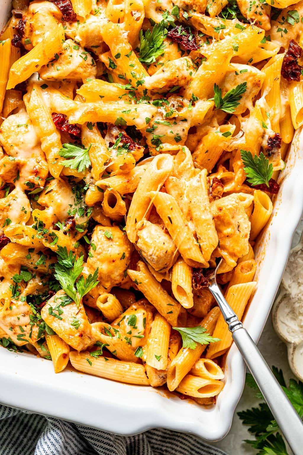 Baked penne pasta with chicken, melted cheese, and sun-dried tomatoes, garnished with fresh parsley.