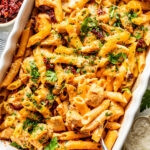 Baked penne pasta with chicken, melted cheese, and sun-dried tomatoes in a white casserole dish.
