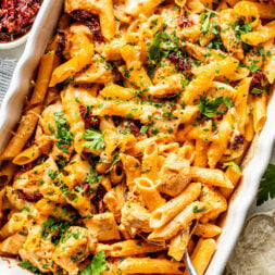 Baked penne pasta with chicken, melted cheese, and sun-dried tomatoes in a white casserole dish.