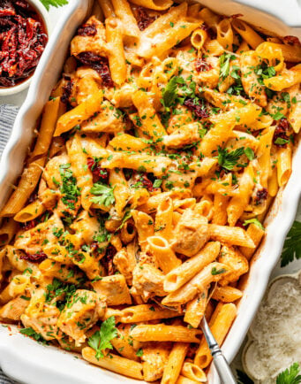 Baked penne pasta with chicken, melted cheese, and sun-dried tomatoes in a white casserole dish.