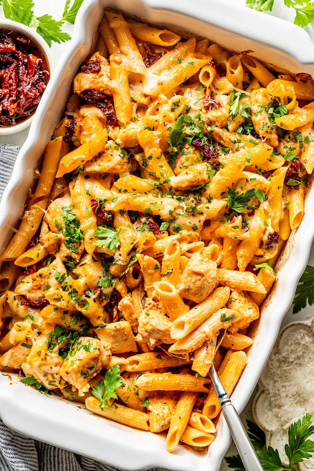 Baked penne pasta with chicken, melted cheese, and sun-dried tomatoes in a white casserole dish.