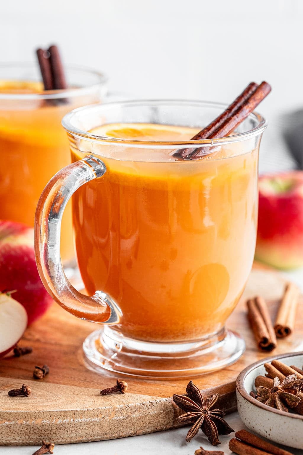 Glass mug of hot apple cider garnished with an orange slice and a cinnamon stick.