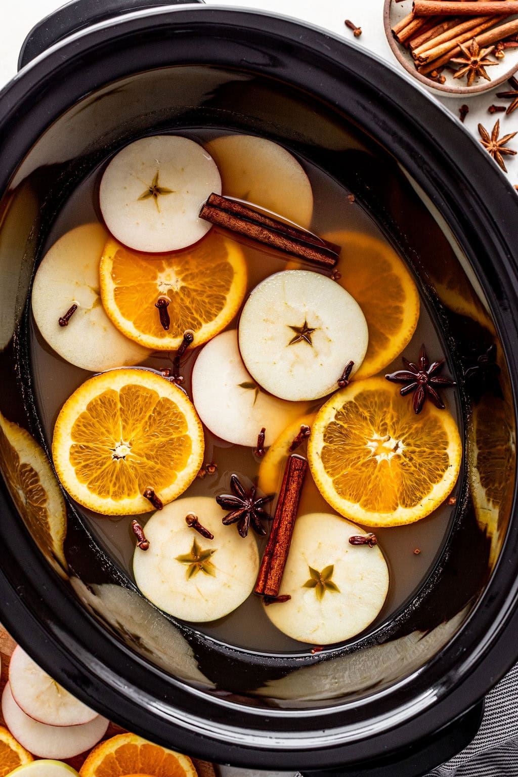 Slow cooker filled with apple cider, sliced apples, orange slices, cinnamon sticks, star anise, and whole cloves.