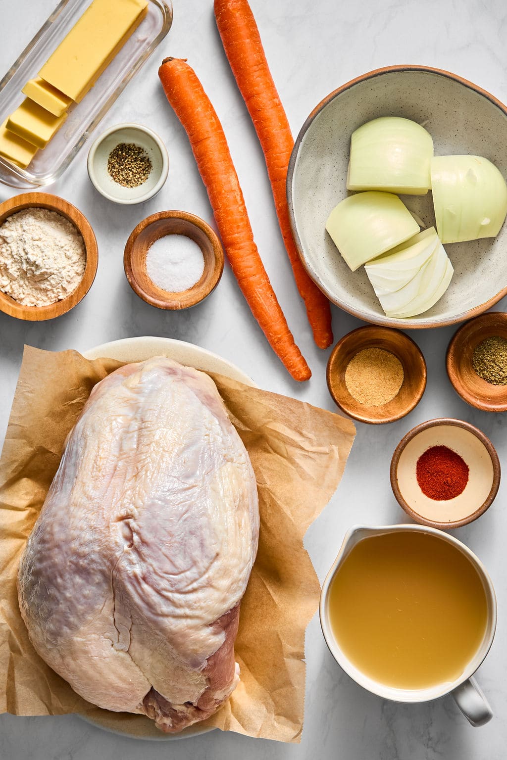 Raw turkey breast, carrots, onion chunks, butter, broth, and small bowls of flour and spices arranged on a surface.