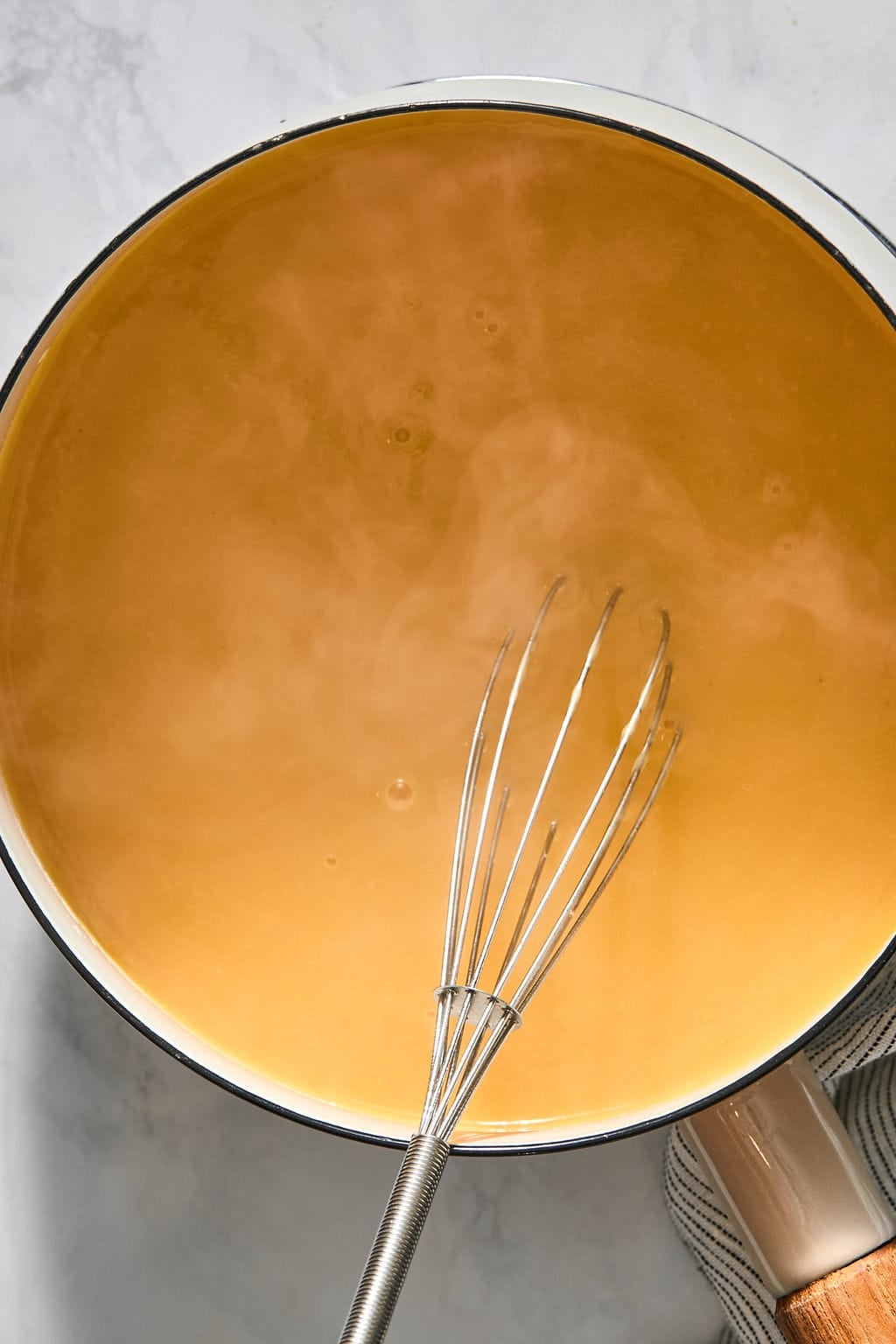 A metal whisk sits in a pot of steaming orange soup.