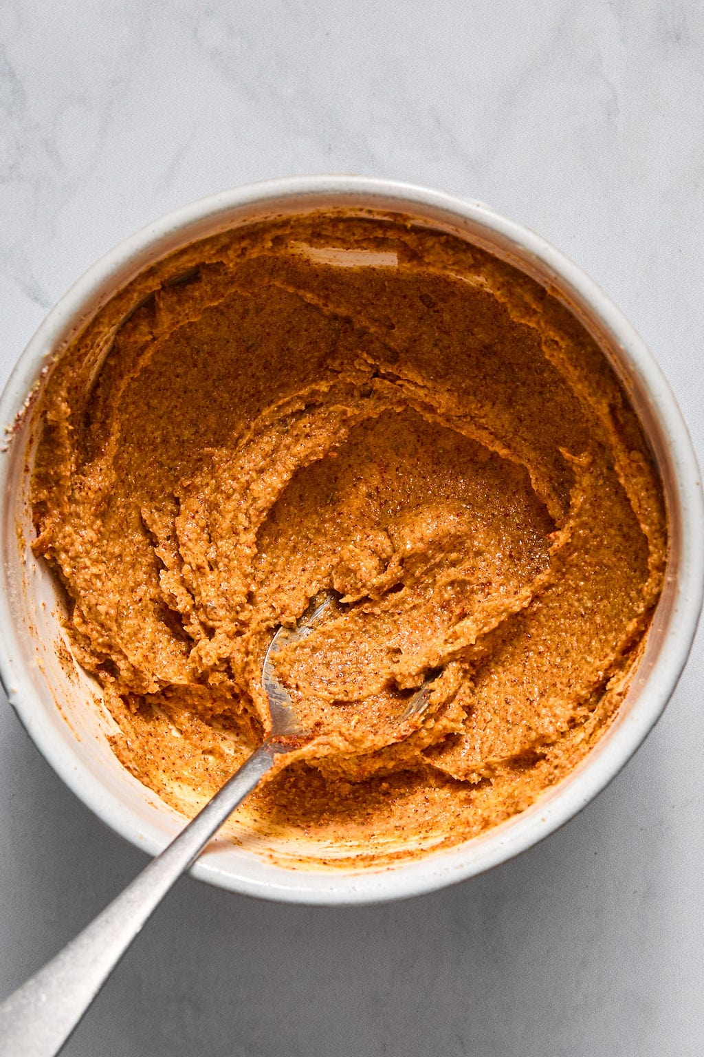 A metal spoon resting in a white bowl filled with textured, orange-brown paste.