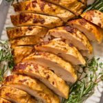 Sliced roasted turkey breast garnished with fresh rosemary and thyme on a white platter.