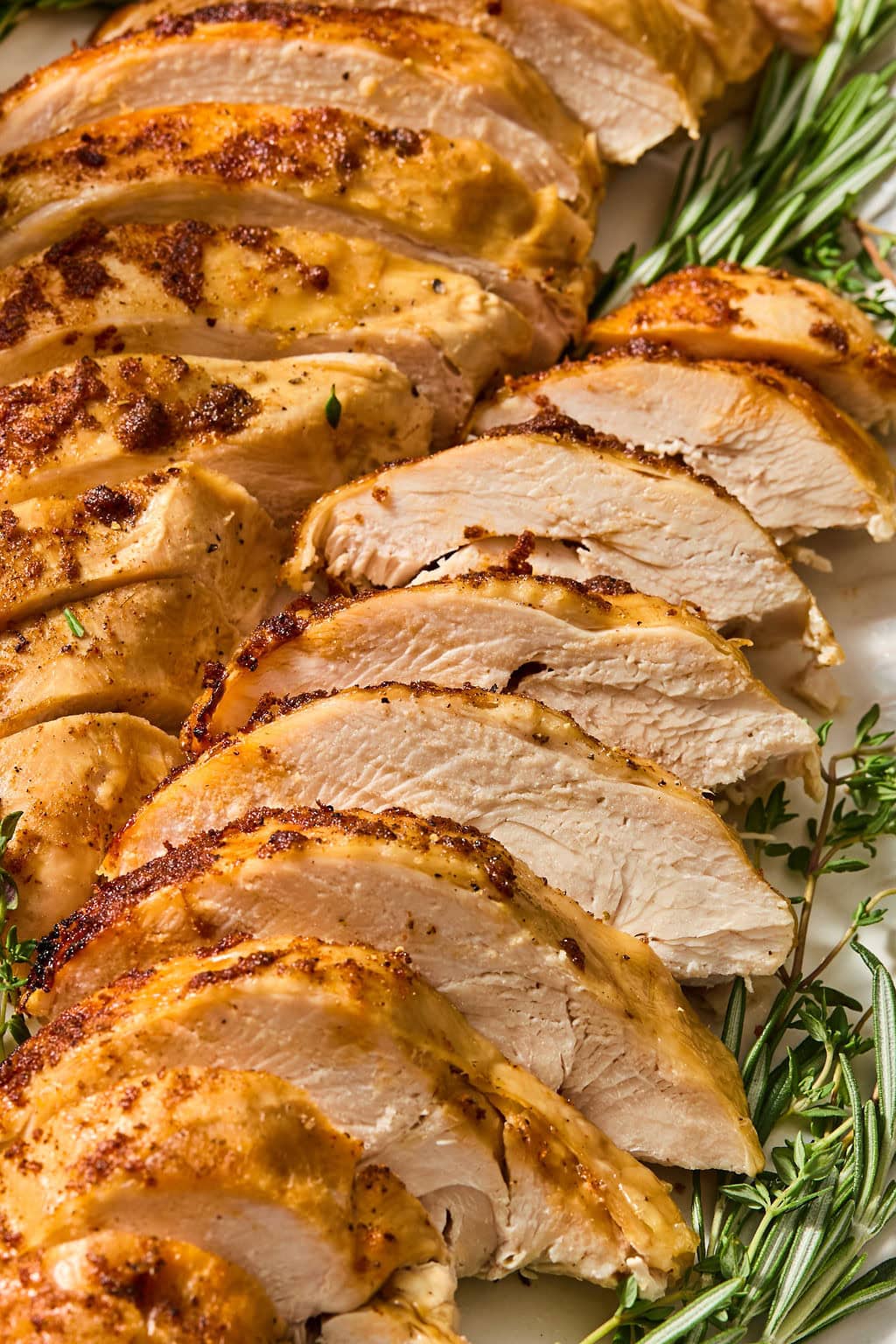 Sliced roasted turkey breast garnished with sprigs of fresh rosemary and thyme.