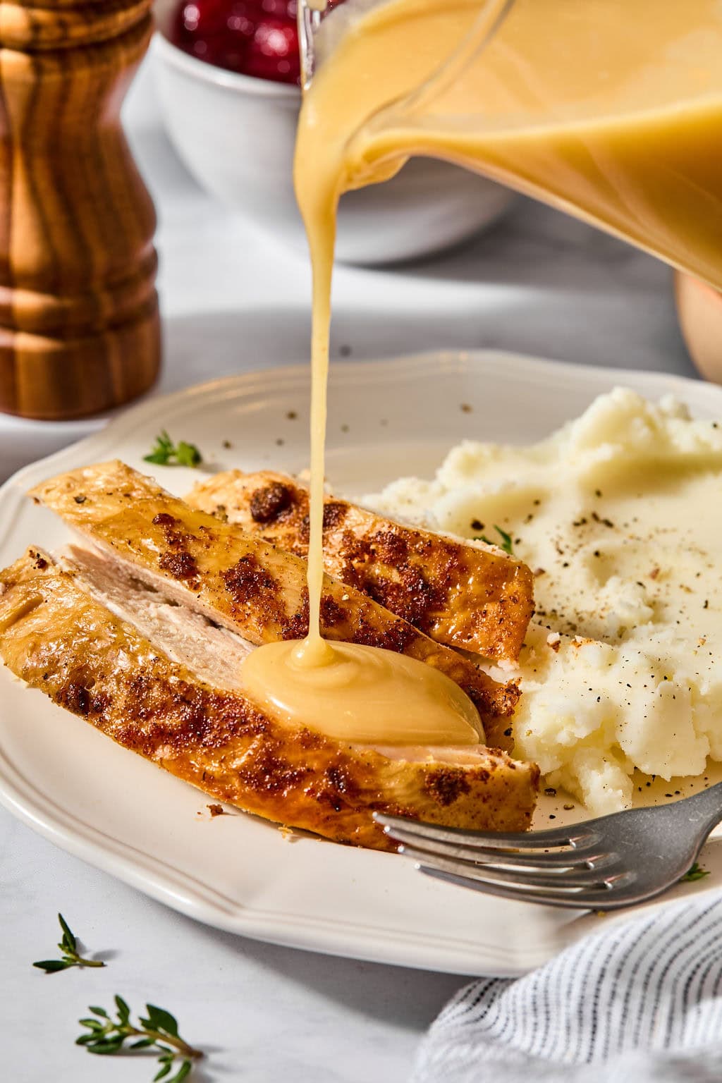 Gravy being poured over sliced turkey breast next to a serving of mashed potatoes.