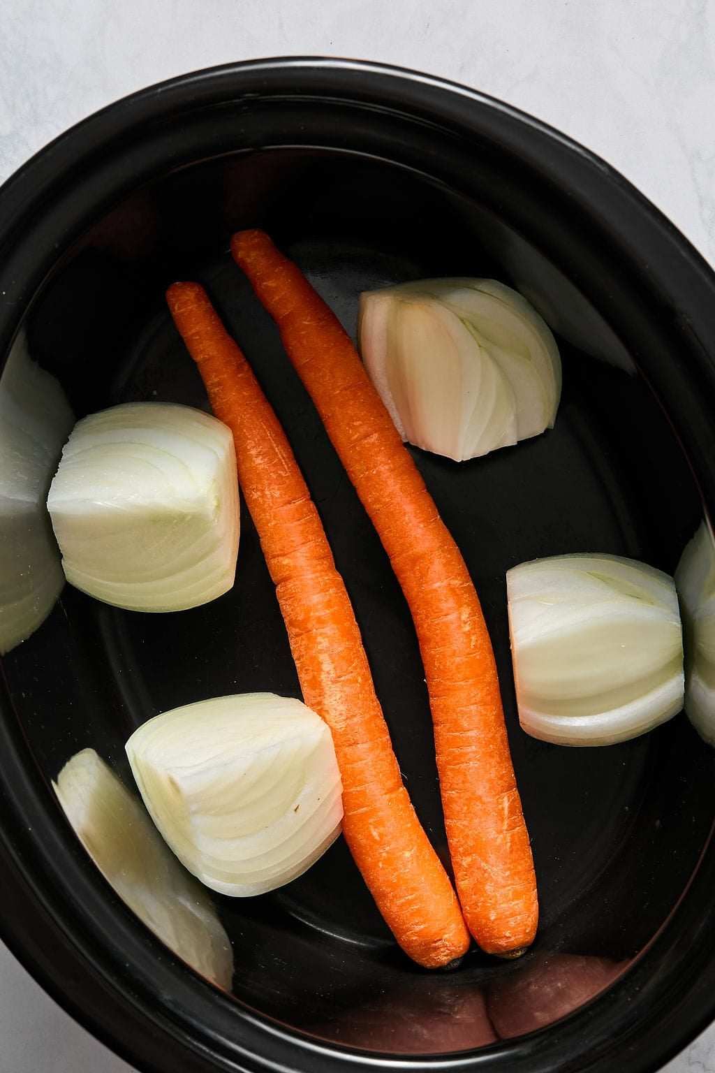 Two whole carrots and four onion wedges in a black slow cooker insert.