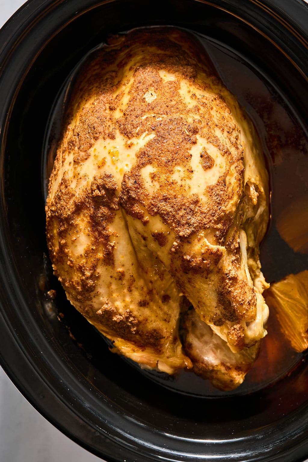 Seasoned turkey breasts in a black slow cooker.