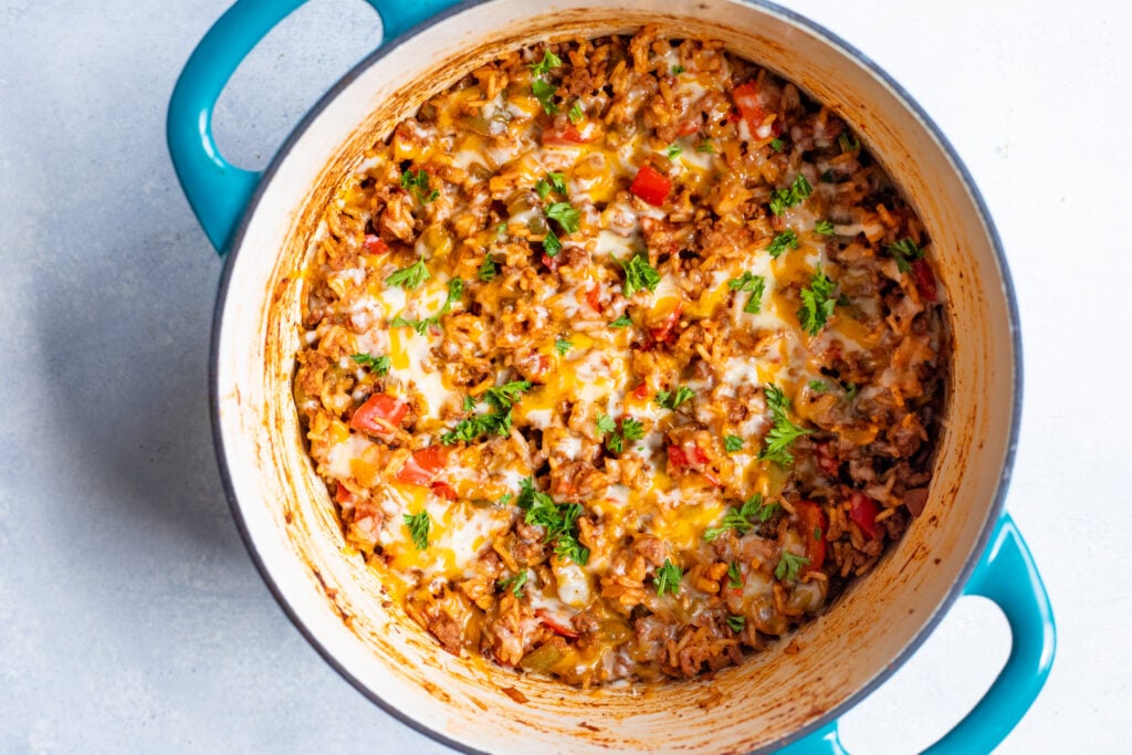 Cheesy rice and meat casserole in a teal Dutch oven, garnished with fresh parsley.