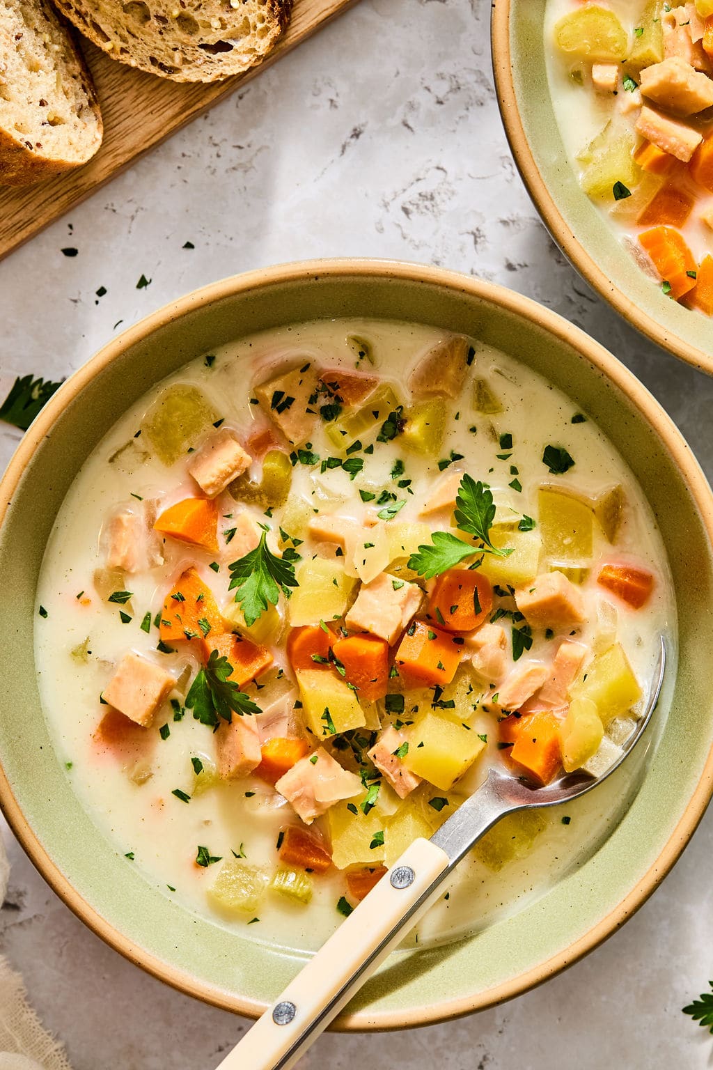 Creamy soup with diced turkey, potatoes, and carrots in a green bowl with a spoon.